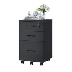 a black filing cabinet with three drawers on wheels and flowers in the top right corner