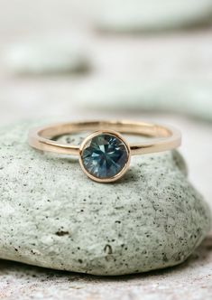 a gold ring with a blue topazte sits on a rock in front of some rocks