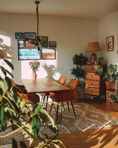 a dining room table surrounded by potted plants and pictures on the wall above it