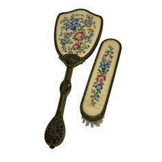 two antique style hair brushes with floral designs on the sides, one being held by a metal handle