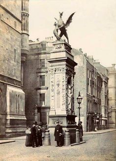 an old black and white photo of people standing in front of a statue on the street