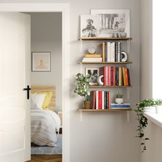 a book shelf with books and plants on it next to a bed in a bedroom