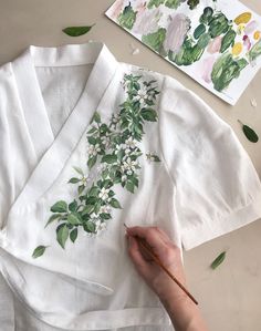 a person is painting flowers on a white shirt with green leaves and watercolors