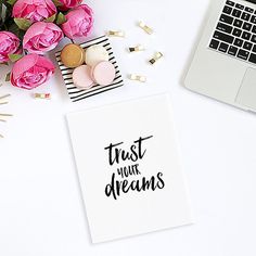 a desk with pink flowers and a laptop on it next to a notepad that says, trust your dreams