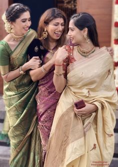 three women standing next to each other in sari and holding something up with their hands