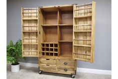 a large wooden cabinet with wine bottles on it's doors and shelves in front of a potted plant