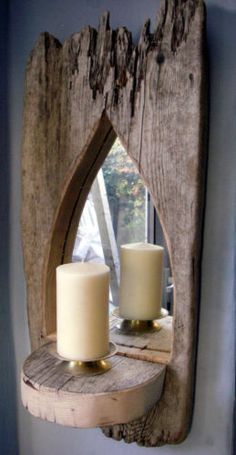 two white candles are sitting on a wooden shelf in front of a window with an arch