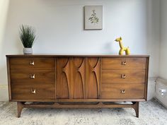 a wooden dresser with two plants on top of it and a giraffe figurine in the background