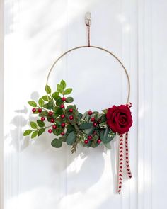 a wreath with red berries and greenery hangs on a door handle in front of a white wall