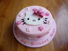 a pink hello kitty birthday cake on a wooden table