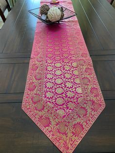 a long table with pink and gold runner on it's centerpiece, in the middle of a dining room