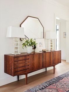 a room with a dresser, mirror and lamp on it's sideboard next to a rug