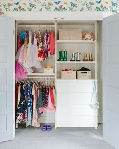 an open closet with clothes and shoes hanging on the shelves, next to a wallpapered ceiling