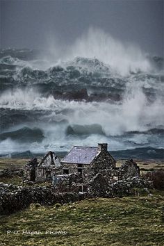 an old stone house in the middle of a field with large waves crashing over it