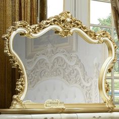 an ornate gold framed mirror sitting on top of a white table next to a window