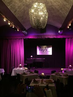 a room filled with tables covered in white tablecloths and purple draping