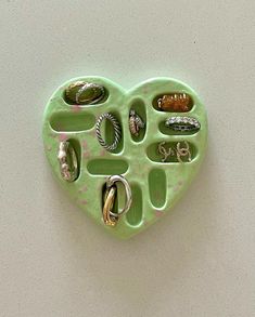 a green heart shaped tray with rings and jewelry in it on a white wall background