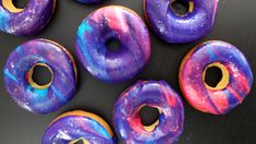 there are many donuts with purple and blue icing on them, all together