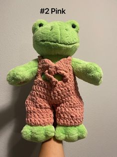 a hand holding a green and pink frog stuffed animal