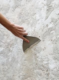 a person holding a shovel in front of a white wall with peeling paint on it