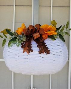 a white wicker basket with flowers and leaves on it hanging from the side of a door