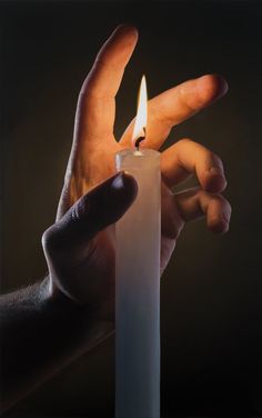 a hand holding a lit candle in front of a black background with the light coming from it