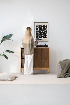 a woman standing in front of a white wall next to a wooden cabinet with a record player on it