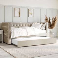 a white bed sitting on top of a wooden floor next to a wall with pictures above it