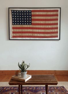 an american flag hanging on the wall above a coffee table with a potted plant