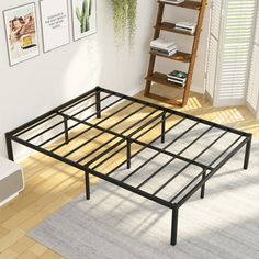 a metal bed frame in a room with white walls and wooden flooring next to a book shelf