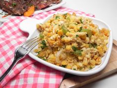 a white bowl filled with rice and vegetables on top of a wooden cutting board next to a fork