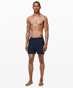 a shirtless man standing in front of a white background wearing blue trunks and no shirt