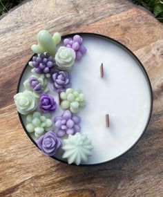 a white candle with purple and green flowers on it sitting on top of a wooden table