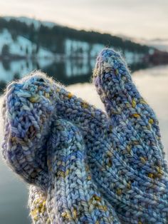 a person's hand wearing knitted mittens in front of a body of water