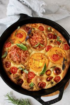 a pizza with tomatoes and herbs in a cast iron skillet on a white table