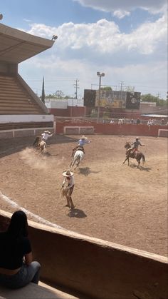 some people are riding horses in an arena with other animals on the ground and one person is watching