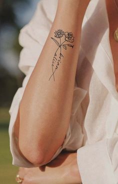 a woman's arm with a flower tattoo on her left forearm and the words, birth month flowers tattoo written in cursive