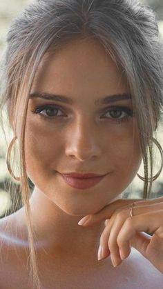 a close up of a person with very large hoop earrings on her head and one hand near her face