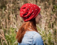 a woman wearing a red hat with white polka dots in front of some tall grass