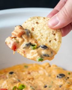 a hand holding a tortilla chip over a bowl of quesadilla dip