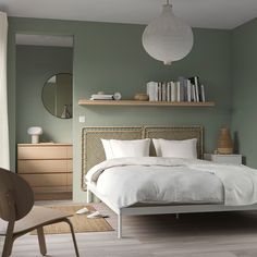 a bed with white linens and pillows in a green room next to a book shelf