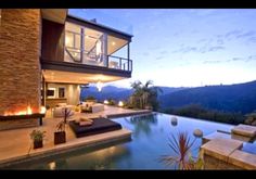 an outdoor living area with fireplaces and couches next to a swimming pool at dusk