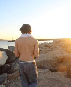 a man standing on top of a rock covered beach next to the ocean at sunset