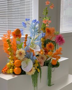 a vase filled with lots of different types of flowers and fruit in front of a window