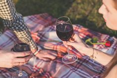 two people toasting wine glasses on a blanket