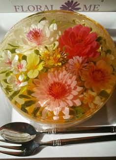 a glass bowl filled with flowers next to two spoons