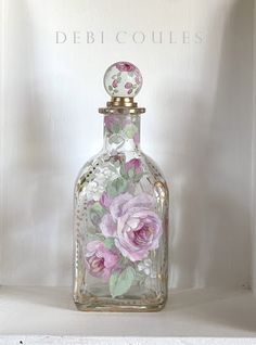 a glass bottle with pink flowers painted on the front and sides, sitting on a shelf