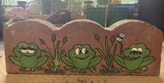 two green frogs sitting on top of a rock with grass and flowers painted on it