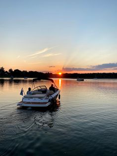 a boat floating on top of a lake next to the sun setting in the sky