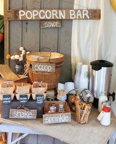 a table topped with lots of food next to a wooden sign that says popcorn bar